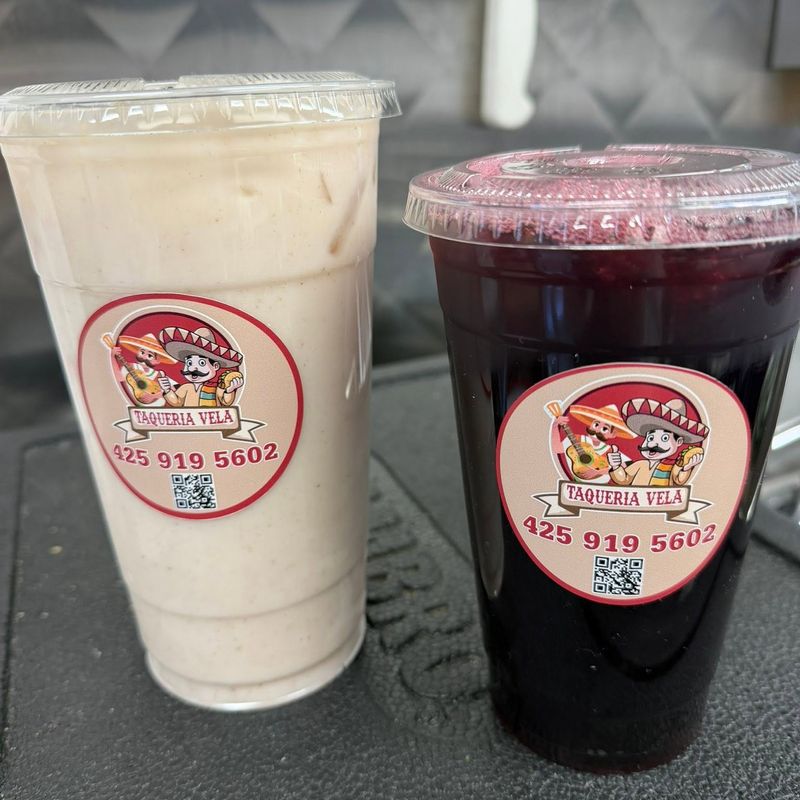 Two large cups of aguas frescas—horchata and jamaica—with Taquería Vela stickers