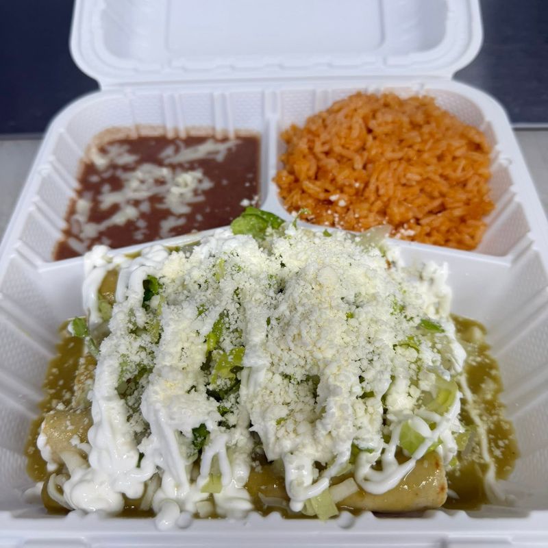 Enchiladas in green sauce topped with crema and queso, served with Mexican rice and beans