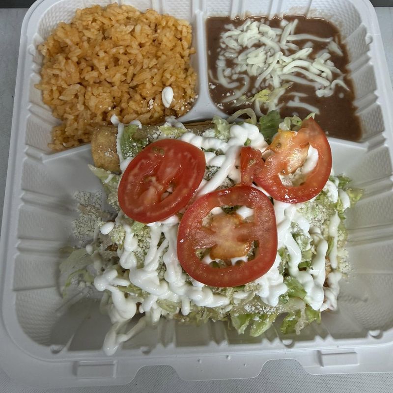 A generous takeout plate with Mexican rice, beans, lettuce, tomato and crema