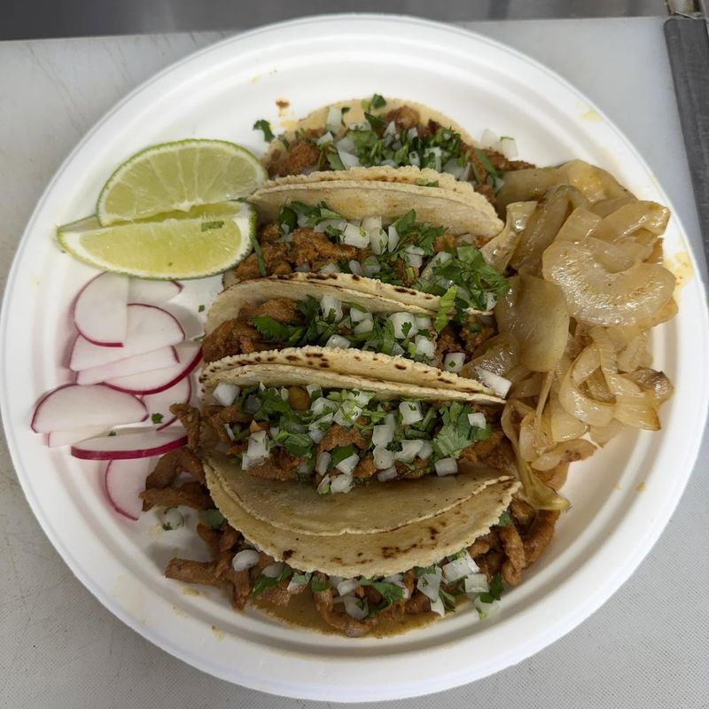 A plate of street tacos topped with onion and cilantro, served with lime, radish and grilled onions