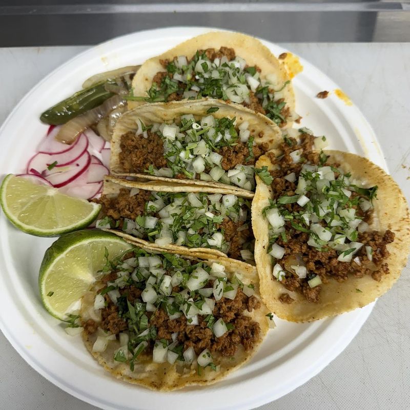 Four street tacos on handmade tortillas topped with onion and cilantro, with lime and radish